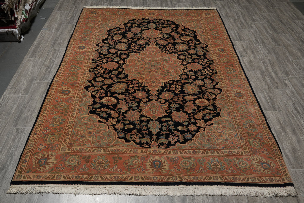 A traditional oriental area rug with a black central medallion and an orange-brown border, laid out on a gray wood-look floor.