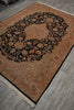 Load image into Gallery viewer, An oriental-style area rug with a complex floral and medallion pattern, shown laid out on a gray wood-look floor. The rug features a black central field surrounded by rust-orange, beige, and muted blue-green details, with a fringed edge.