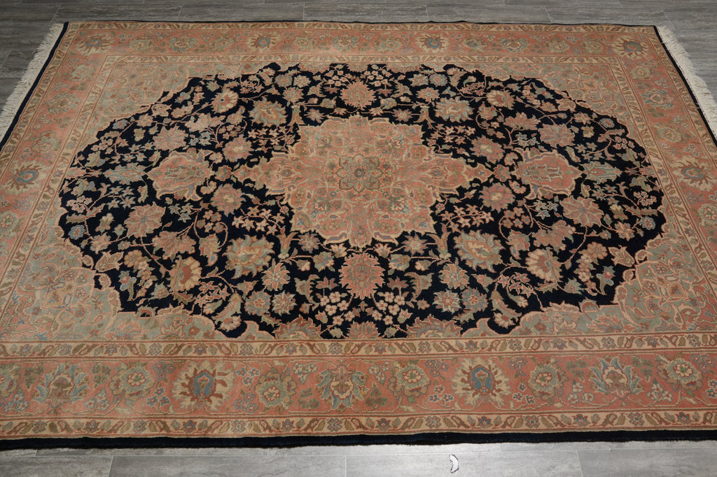 A large traditional oriental area rug with a central medallion and floral pattern, shown laid flat on a gray tiled floor. The rug features a dusty rose and beige background with a prominent black central field and intricate floral motifs.
