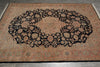 Load image into Gallery viewer, A large traditional oriental area rug with a central medallion and floral pattern, shown laid flat on a gray tiled floor. The rug features a dusty rose and beige background with a prominent black central field and intricate floral motifs.