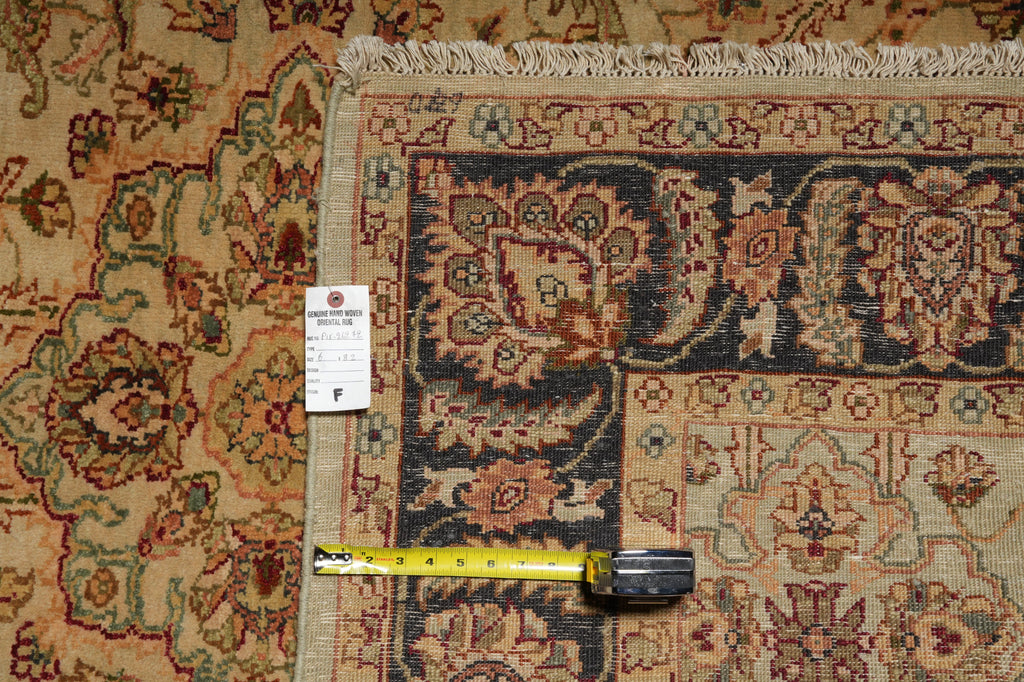 A close-up of a patterned area rug corner with a white size tag and a yellow tape measure laid across the border, showing the rug's detailed floral and geometric design in beige, navy, and rust tones.