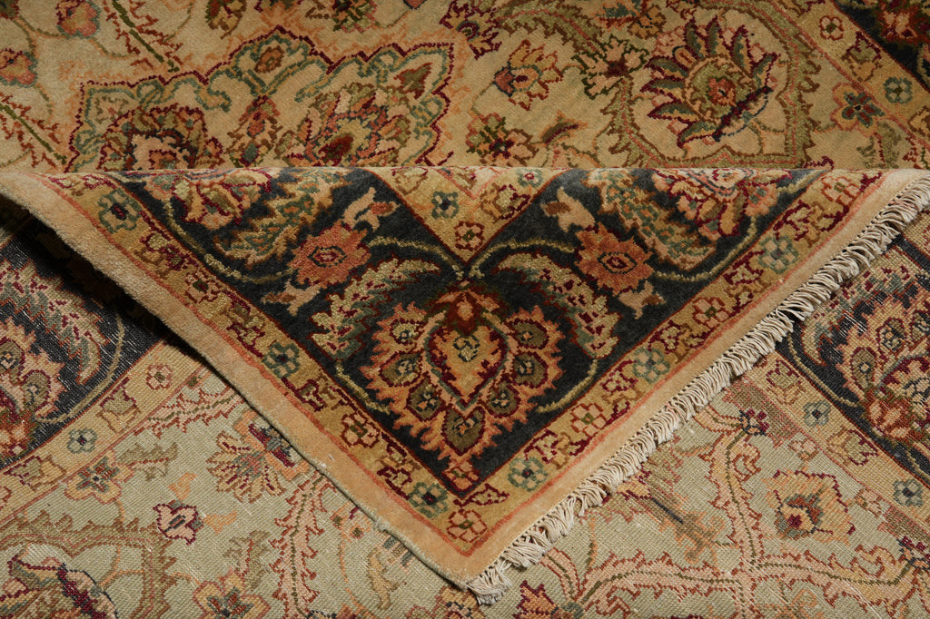 A close-up of an ornate traditional rug corner showing a beige and navy blue patterned design with fringed edges.