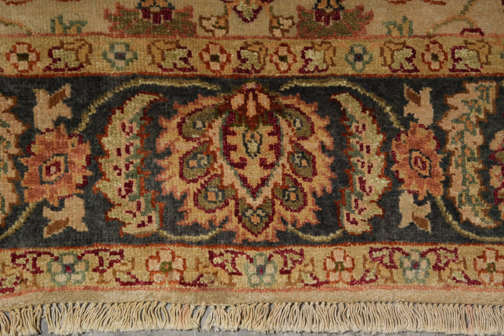 Close-up of an ornate patterned rug with a central floral medallion and fringe along the bottom edge. The design features beige, dark blue, red, and green tones.