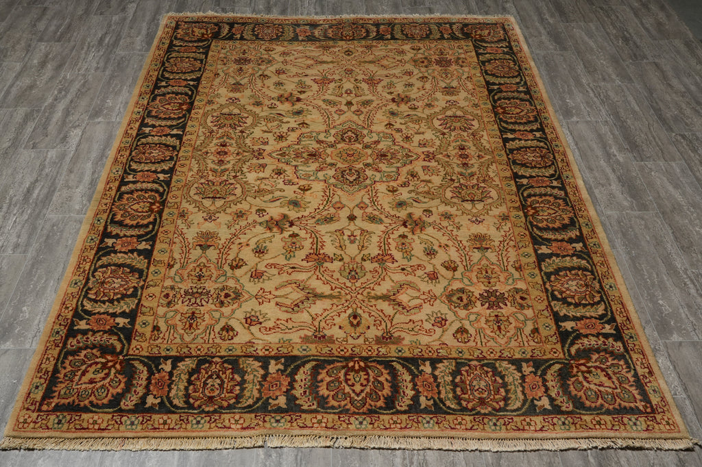 A rectangular traditional area rug with an intricate floral and medallion pattern, featuring a beige center, dark navy borders, and rust-orange accents, laid out on a gray wood-plank floor.