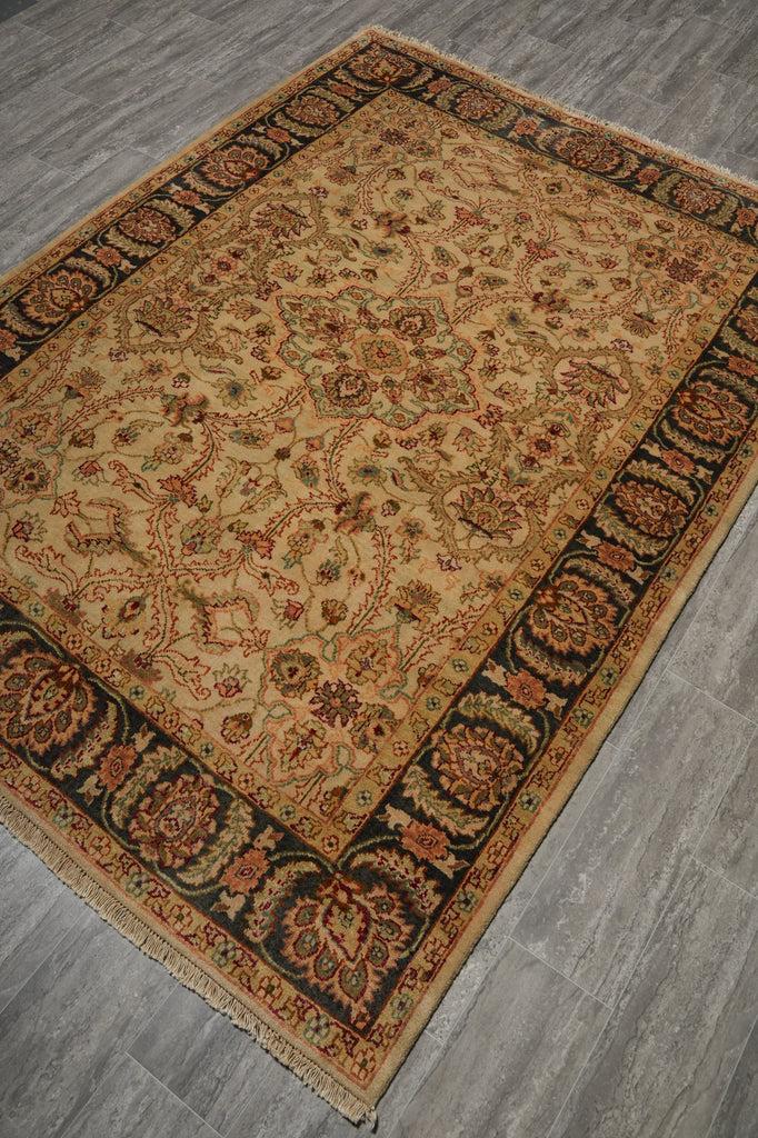 A rectangular traditional area rug with an intricate floral and medallion pattern, shown from an elevated angle on a gray wood-look floor. The rug features a warm beige center field, dark brown borders, and accents of rust red, green, and blue in the detailed pattern.