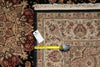 Load image into Gallery viewer, A close-up of a traditional patterned area rug with cream, beige, red, and black tones, shown with a yellow tape measure and a white product tag placed on it for scale.