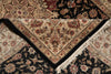 Load image into Gallery viewer, A close-up of a traditional patterned rug with a beige central field, black borders, and white fringe, layered over other dark floral rugs.
