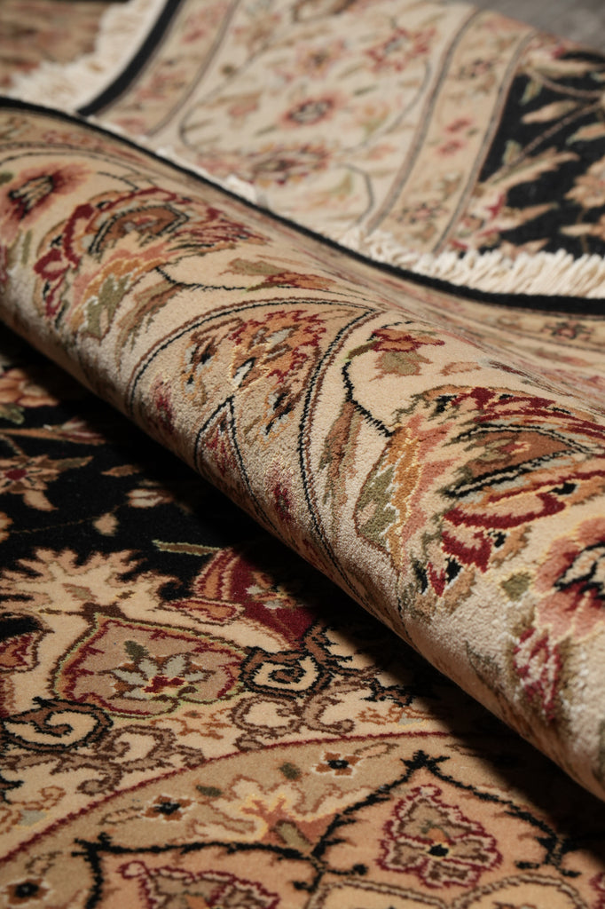 A close-up of a rolled section of a traditional oriental rug showing its detailed floral and geometric patterns in beige, red, green, and black.