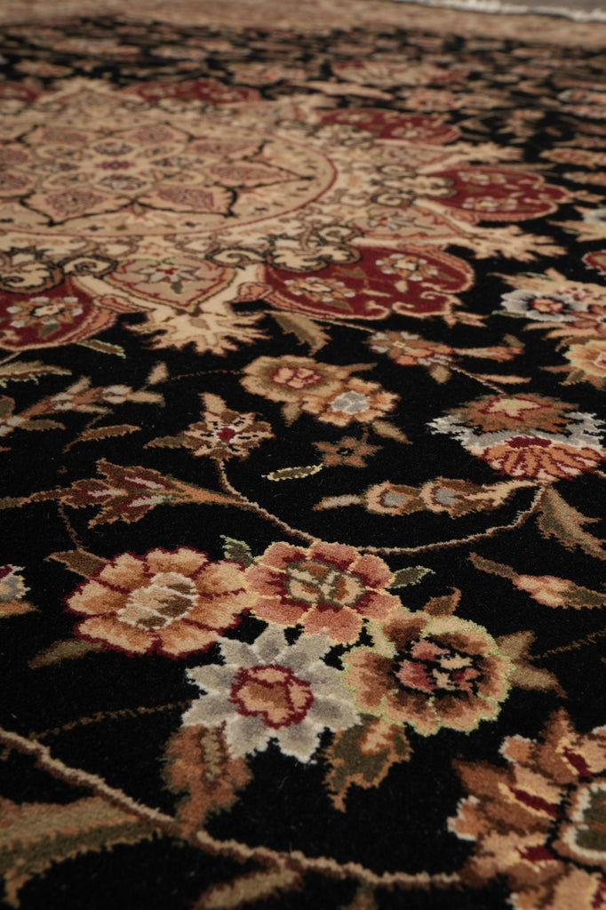 Close-up of a traditional oriental-style area rug with a black background and floral motifs in beige, red, and cream.