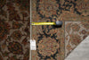 Load image into Gallery viewer, A close-up of a patterned area rug with a vintage-style floral and medallion design in dark navy, rust red, beige, and brown tones. A yellow tape measure is laid horizontally across the rug to indicate scale, and a white inventory tag is attached near the lower left.
