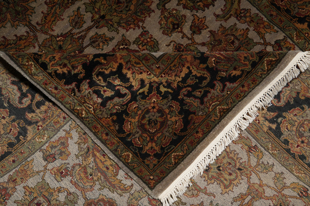 A close-up of an ornate patterned rug corner showing a dark navy central field with floral motifs in rust, gold, olive, and beige, bordered by cream fringe and additional patterned sections.
