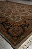Load image into Gallery viewer, An ornate traditional area rug with a complex floral and vine pattern, shown folded to display its corner, border, and cream-colored fringe on a gray floor.