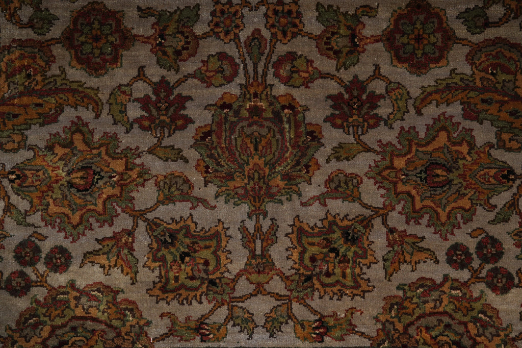 A close-up of an ornate traditional patterned rug with a central floral medallion and repeating motifs in muted brown, rust orange, olive green, and beige tones.