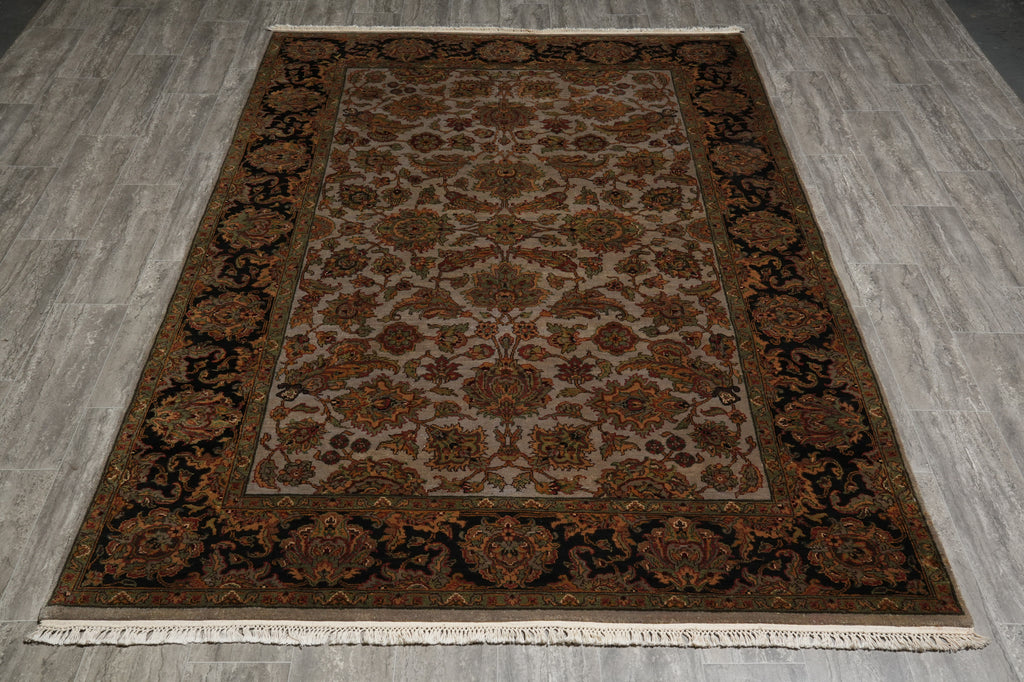A rectangular traditional area rug with an intricate floral and geometric pattern, displayed flat on a gray wood-look floor. The rug features a beige center field, a dark brown border, and cream-colored fringe at the top and bottom.