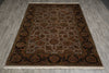 Load image into Gallery viewer, A rectangular traditional area rug with an intricate floral and geometric pattern, displayed flat on a gray wood-look floor. The rug features a beige center field, a dark brown border, and cream-colored fringe at the top and bottom.