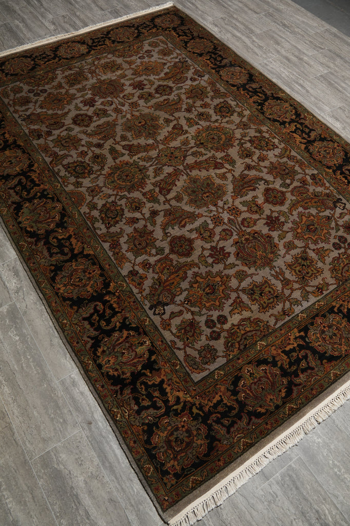 A traditional oriental-style area rug with an intricate floral pattern, shown laid out on a gray wood-look floor. The rug features a dark brown and black patterned border and a beige center field with warm rust and brown floral motifs.