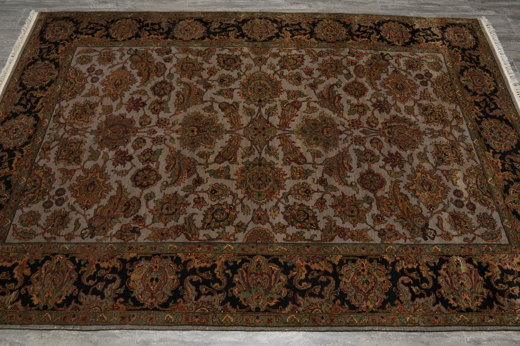 An oriental-style area rug with an intricate floral and medallion pattern, featuring a beige center field, dark brown and black borders, and rust-orange accents, laid out on a gray floor.