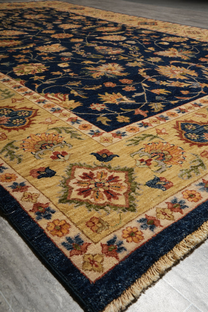 A traditional oriental area rug with a navy blue field, beige border, and multicolor floral motifs, shown laid out on a gray floor.