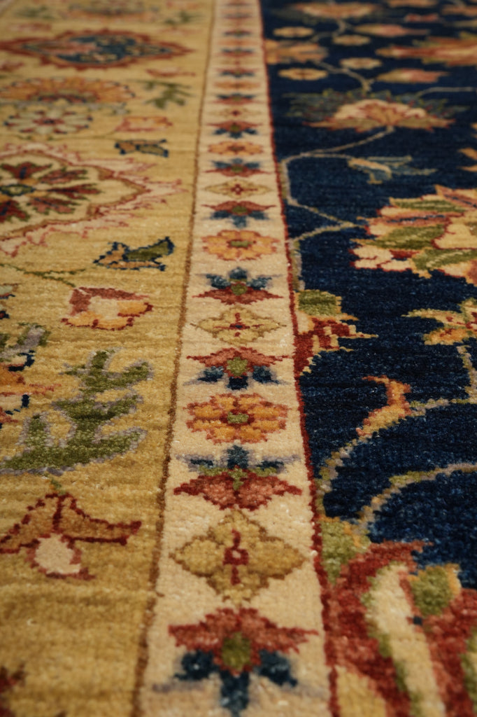 Close-up of a traditional patterned area rug showing a cream central border with floral motifs and a dark navy blue field with floral and vine patterns.