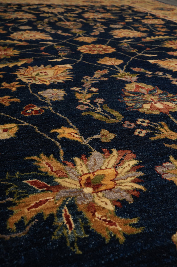 A close-up view of a traditional area rug featuring a dark navy blue background with large floral motifs in beige, gold, rust red, and muted green.