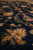 Load image into Gallery viewer, A close-up view of a traditional area rug featuring a dark navy blue background with large floral motifs in beige, gold, rust red, and muted green.