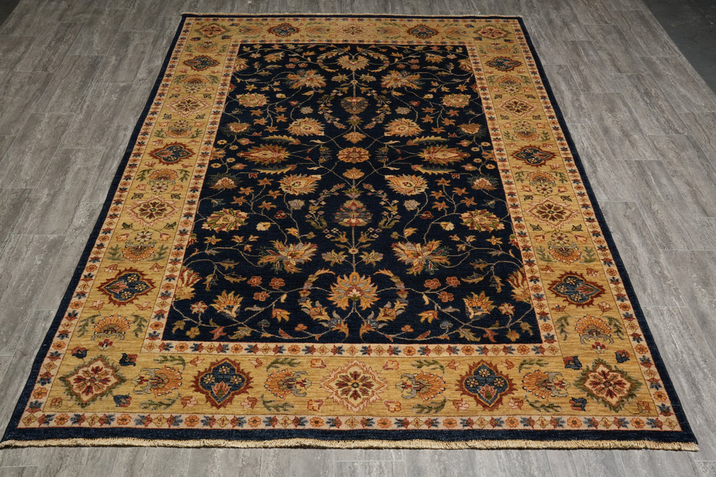 A rectangular area rug with an ornate traditional floral pattern, featuring a dark navy blue center field and a wide mustard-gold border, laid out on a gray wood-look floor.
