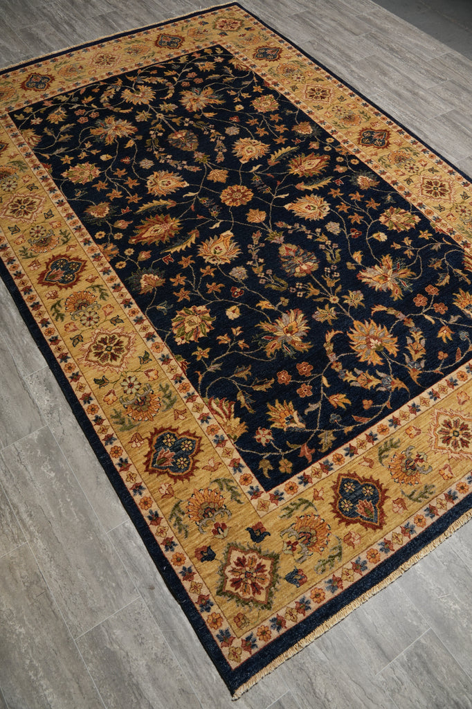 A rectangular area rug with a dark navy blue center field and an ornate golden-yellow border, shown laid out on a gray wood-look floor.
