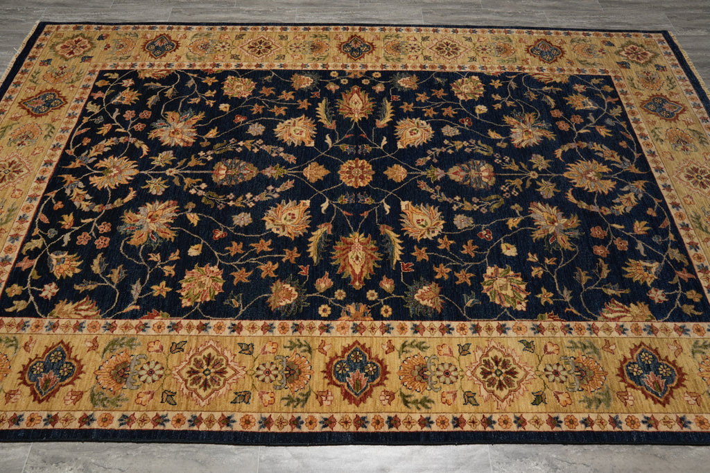 A rectangular area rug with an intricate traditional floral pattern, featuring a dark navy blue center field and ornate beige borders with gold, orange, and green accents.
