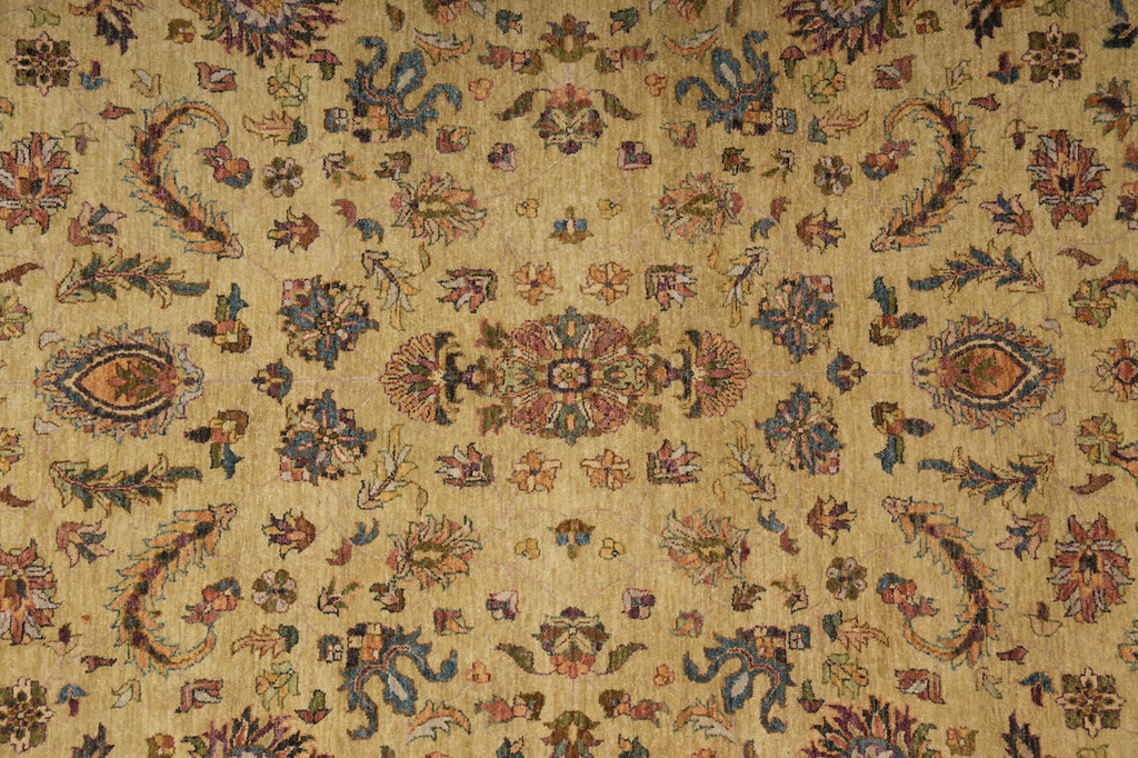 A close-up of an ornate patterned textile or rug with a warm beige/tan base and intricate floral, paisley, and medallion motifs in muted blue, rust red, and brown tones.