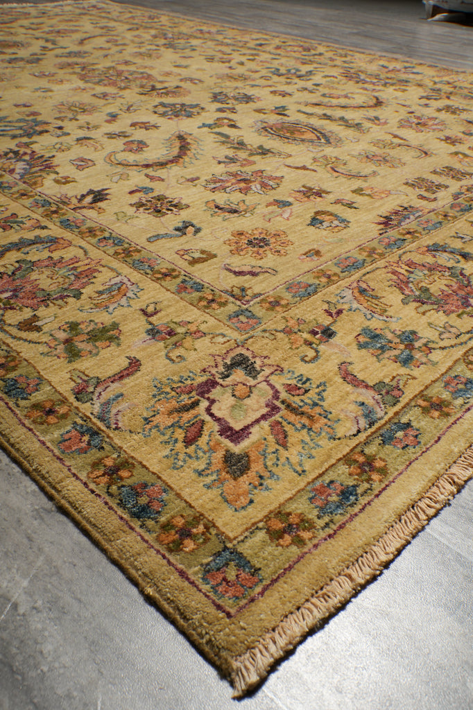 A traditional oriental area rug with a warm mustard yellow base and an intricate floral and medallion pattern in muted red, blue, green, and brown, shown laid out on a gray concrete floor.