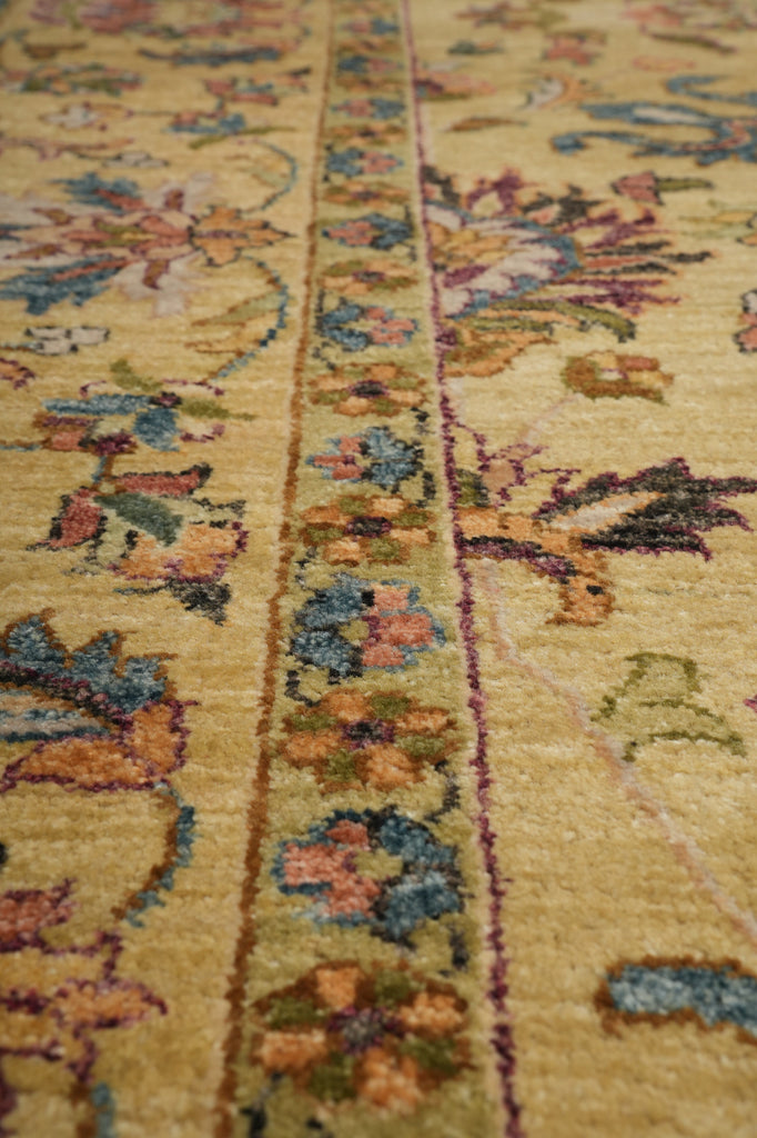 Close-up of a traditional patterned area rug with a warm beige background and floral motifs in muted blue, green, orange, and purple tones.