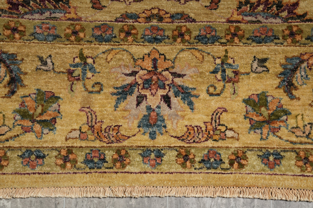 A close-up of a traditional patterned rug with a warm mustard yellow base, featuring floral motifs and a central medallion in muted blue, green, and terracotta tones, finished with a fringed edge.