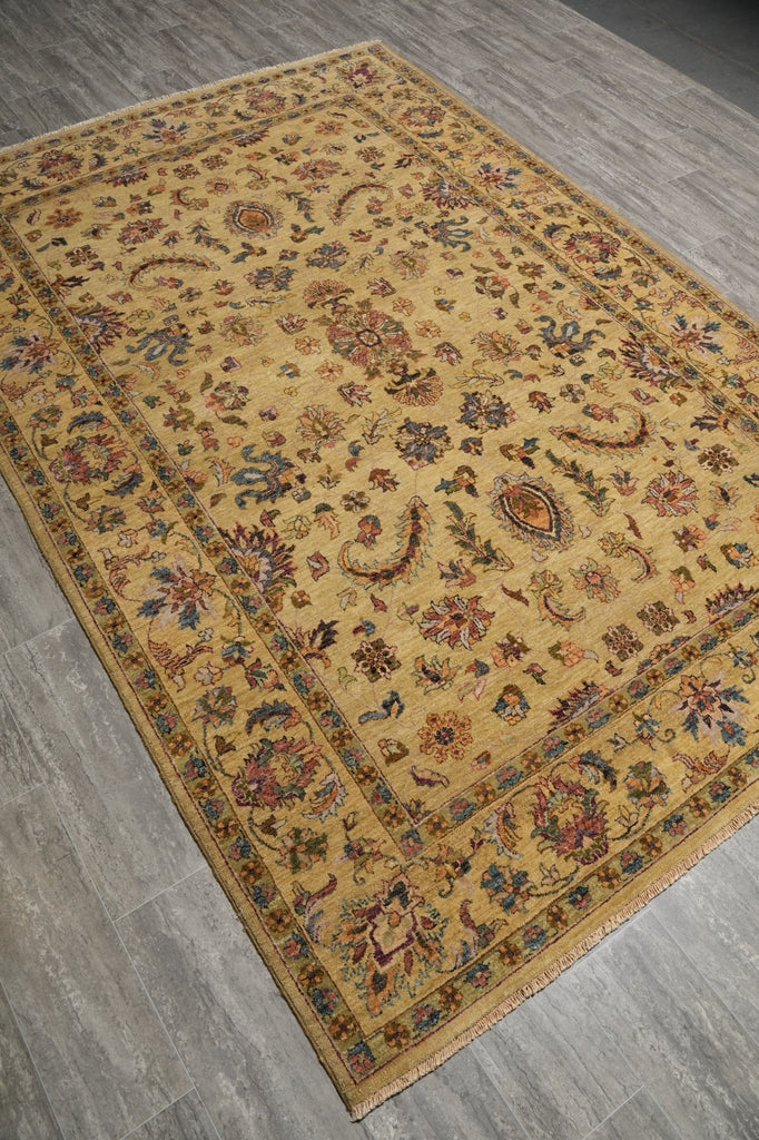 A rectangular vintage-style area rug with an intricate floral and paisley pattern in warm beige, gold, brown, and muted blue tones, laid out on a gray wood-look floor.