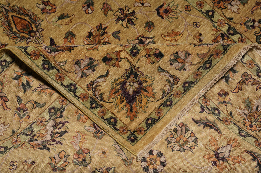 A close-up of a folded area rug with a traditional floral pattern in beige, brown, green, and muted orange tones.