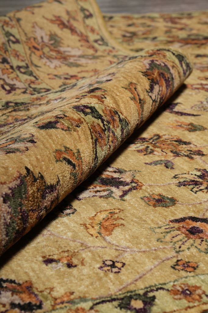A close-up of a rolled area rug showing its detailed floral pattern in warm beige, brown, and muted green tones.