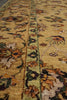Load image into Gallery viewer, A close-up view of an ornate area rug with a warm golden-yellow base, featuring a central vertical border and floral motifs in green, brown, orange, and cream.