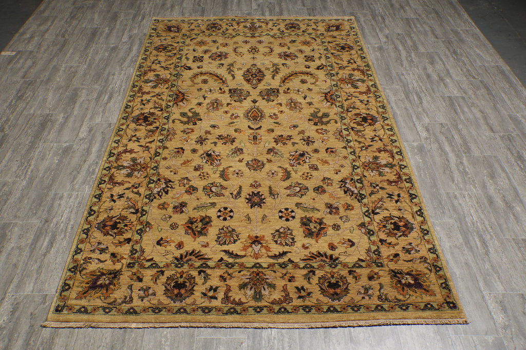 A rectangular area rug with an intricate traditional floral pattern in beige, brown, and muted green, laid out on a gray wood-look floor.