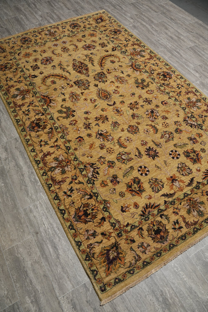A rectangular vintage-style area rug with an intricate floral and paisley pattern, featuring a warm golden-yellow background and dark brown accents, laid out on a gray wood-look floor.