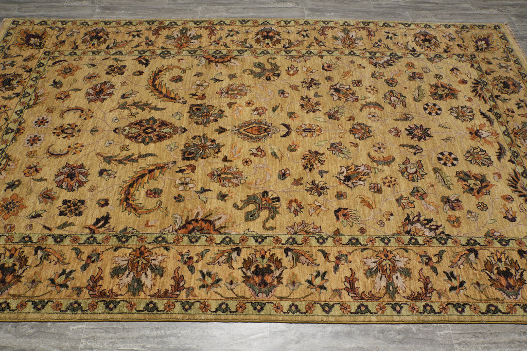 A rectangular area rug with an intricate traditional floral and paisley pattern in shades of beige, brown, and muted green, laid out on a gray tiled floor.