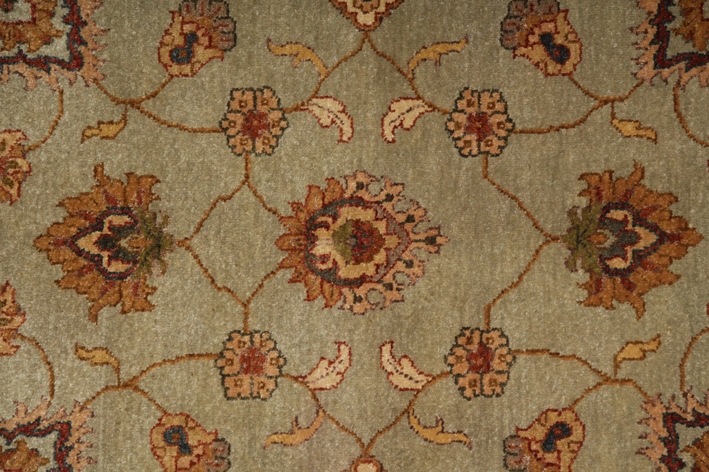 A close-up of a traditional patterned rug with a muted sage green background and floral motifs in brown, rust, beige, and dark accents.