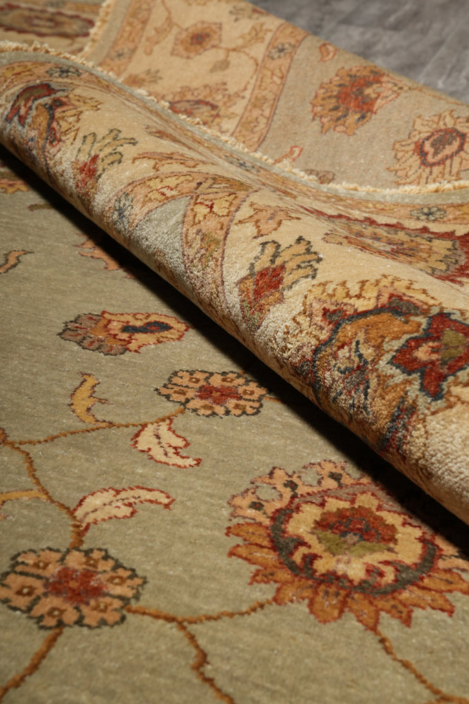 A close-up of a traditional oriental-style area rug with a floral pattern, shown partially rolled to reveal both the patterned top surface and the underside.