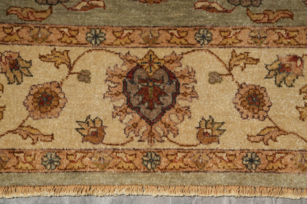 A close-up of an ornate traditional rug with a beige field, floral motifs, and a central medallion, featuring a fringed edge at the bottom.