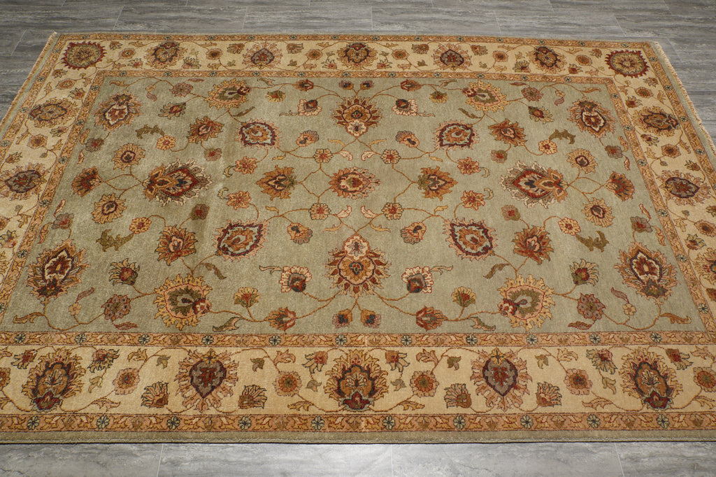 An oriental-style area rug with a beige and sage green base, featuring intricate floral motifs and detailed borders, laid out on a gray tiled floor.
