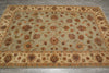 Load image into Gallery viewer, An oriental-style area rug with a beige and sage green base, featuring intricate floral motifs and detailed borders, laid out on a gray tiled floor.