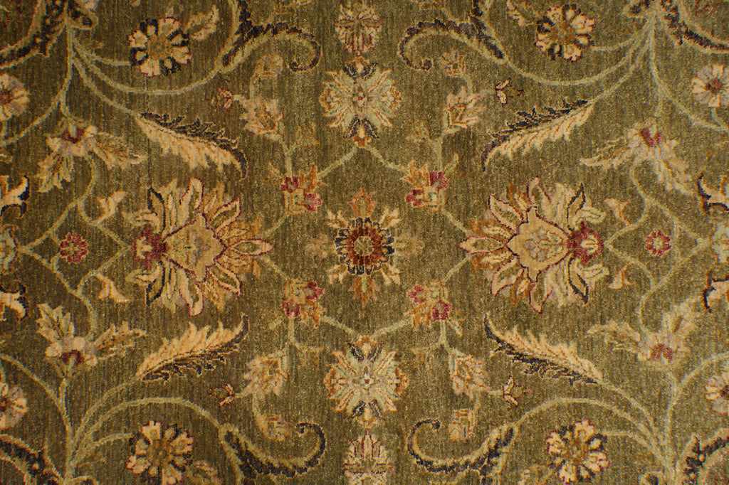 A close-up of an ornate floral patterned fabric or rug in muted olive green, beige, and rust tones, showing detailed woven texture and repeating motifs.