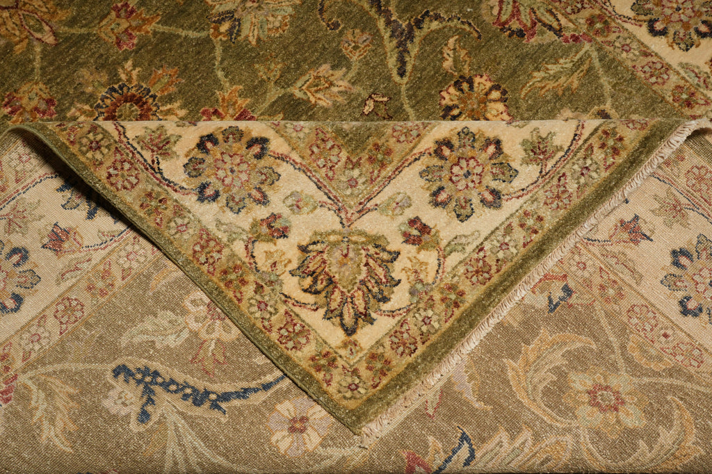 A close-up of a folded area rug showing its intricate floral and vine pattern in beige, olive green, and muted blue tones.