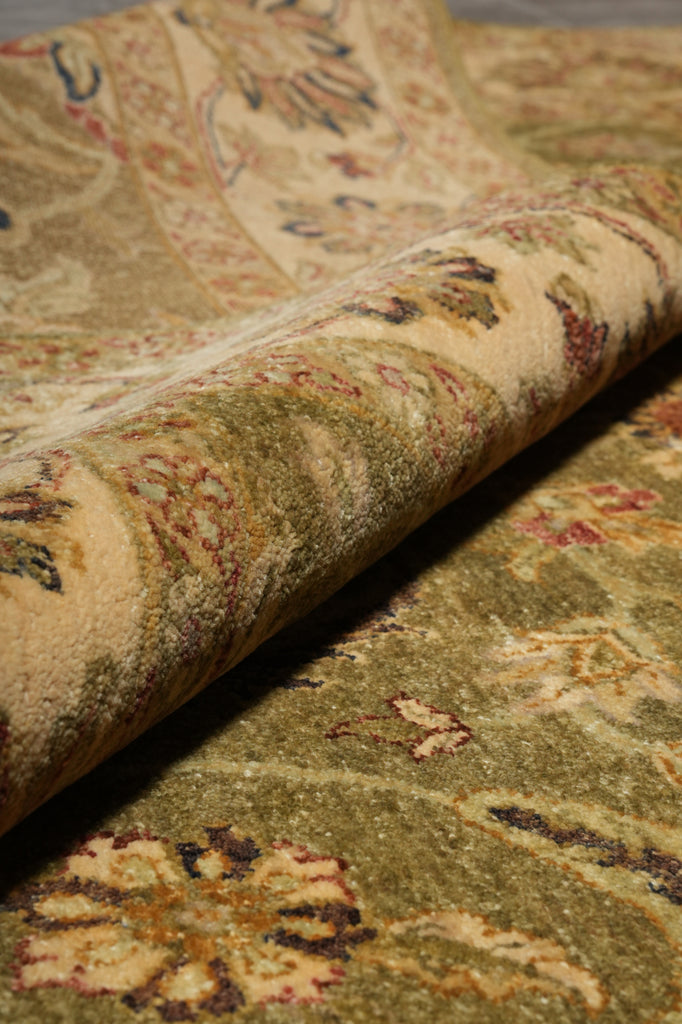 A close-up of a rolled area rug showing its detailed vintage-style floral pattern in muted beige, olive green, and rust red tones.