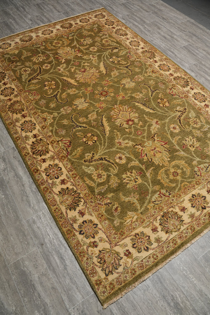 An oriental-style area rug with an intricate floral and vine pattern in olive green, beige, and rust red, shown laid out on a gray wood-look floor.