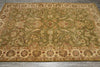 Load image into Gallery viewer, An ornate traditional area rug with a floral and vine pattern in olive green, beige, and rust red tones, laid out on a gray floor.