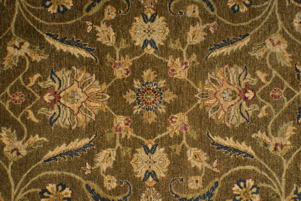A close-up of an ornate floral rug pattern in olive brown, beige, navy blue, and muted red, showing detailed woven texture.